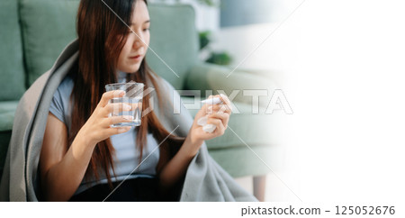 Young Asian woman suffering from flu symptoms, covered with a blanket on a sofa. Concept of illness, healthcare, 125052676