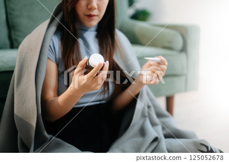 Young Asian woman suffering from flu symptoms, covered with a blanket on a sofa. Concept of illness, healthcare, 125052678