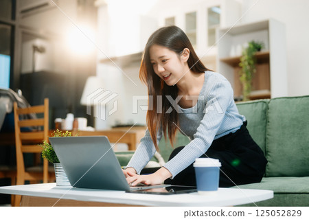 Young Asian woman listening music from headphones and writing note for her work idea in diary book.She in home Young Asian woman listening music from headphones and writing note for her work idea in diary book.She in home 125052829