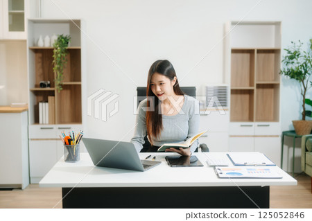 Asian Businesswoman Analyzing Finance on Tablet and Laptop at modern Office Desk 125052846