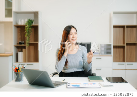 Young beautiful woman typing on tablet and laptop while sitting at the working white table 125052875