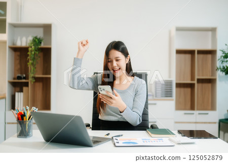 Young beautiful woman typing on tablet and laptop while sitting at the working white table 125052879