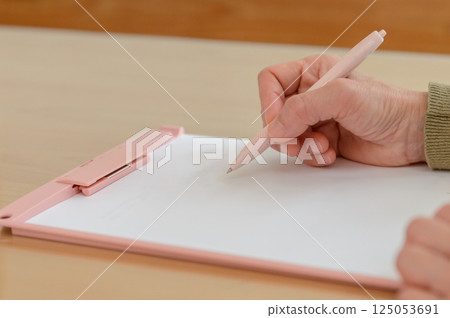 A woman's hand writing on paper with a pen, a woman's hand taking notes, a hand holding a pen, a binder 125053691
