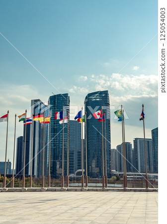 Flags of various nations wave in front of modern skyscrapers. 125054003