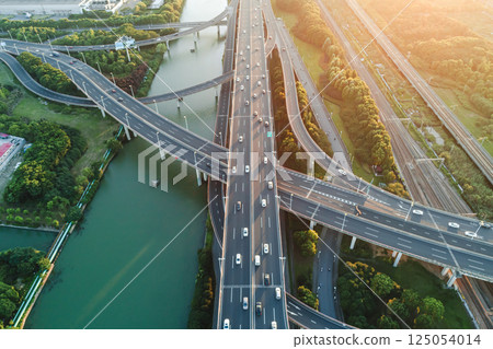 Aerial view of multiple highways intersect above a calm river, surrounded by vibrant greenery. Aerial view of multiple highways intersect above a calm river, surrounded by vibrant greenery. 125054014