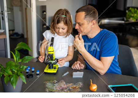 Father and daughter examining various plant samples under a microscope at home. Concept of family science education and botanical exploration 125054208