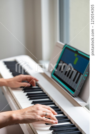 Hands playing a keyboard while following an interactive learning app on a tablet. Technology enables self-education in music without traditional lessons. Hands playing a keyboard while following an interactive learning app on a tablet. Technology enables self-education in music without traditional lessons. 125054305