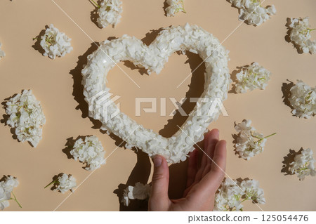 Woman hand Heart made of white lilac flowers on pastel beige background. Still life romantic composition of Valentines day holiday copy space for your text invitation greeting card 125054476