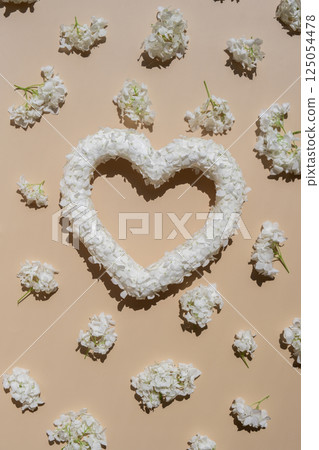 Symbol of love beautiful flower petals in heart shape in beige background. Creative concept of St Valentines day, weeding romantic date or anniversary. Copy space 125054478