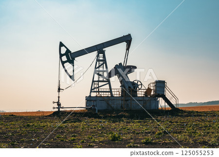 A large oil pump jack operates in an open field, extracting crude oil A large oil pump jack operates in an open field, extracting crude oil 125055253