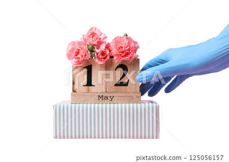 A hand in a blue glove places a wooden calendar showing May 12, isolated on white 125056157
