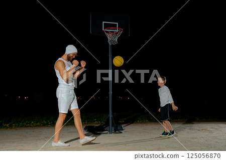 A nighttime basketball game between a child and an adult on an outdoor court under bright lights 125056870