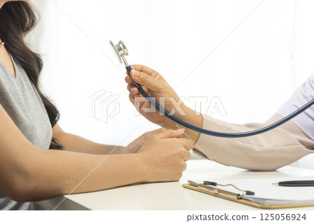 Smiling mature female general practitioner sitting at table and talking to patient 125056924