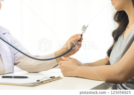 Smiling mature female general practitioner sitting at table and talking to patient 125056925