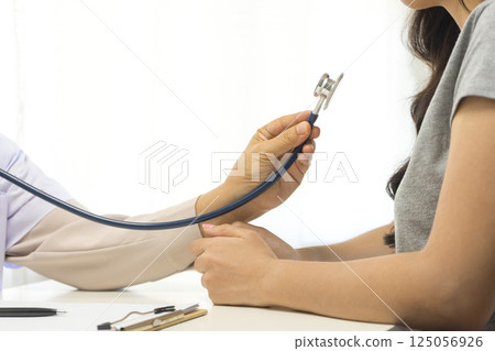 Smiling mature female general practitioner sitting at table and talking to patient 125056926