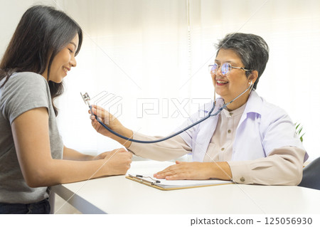Smiling mature female general practitioner sitting at table and talking to patient 125056930