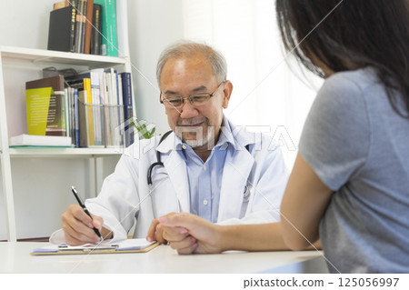 Senior Asian doctor talking with young female patient in hospital. Senior Asian doctor talking with young female patient in hospital. 125056997