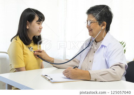 Asian girl and senior psychologist woman having therapy with digital tablet at clinic. Asian girl and senior psychologist woman having therapy with digital tablet at clinic. 125057040