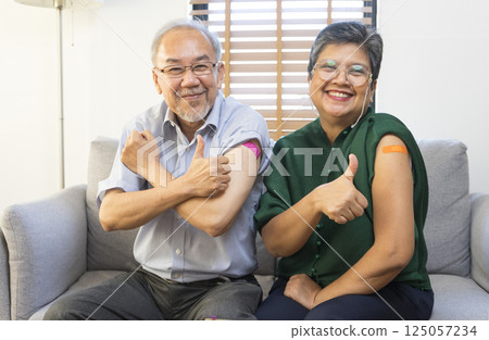 Senior Asian couple get vaccinated with bandage on arm show thumb up sign in living room. Grandfather and grandmother get vaccine. 125057234