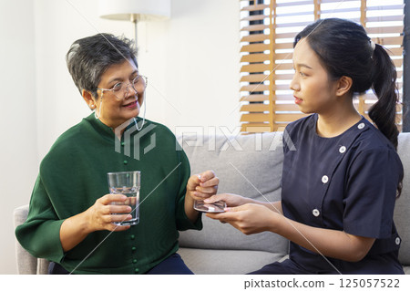 Smiling nurse giving glass of water to senior asian man in nursing home or assisted living facility. 125057522
