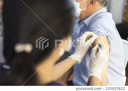 Medical worker perform a vaccine injection to senior Asian man in clinic or medical facility. Medical worker perform a vaccine injection to senior Asian man in clinic or medical facility. 125057622