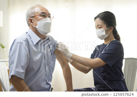 Medical worker perform a vaccine injection to senior Asian man in clinic or medical facility. 125057624