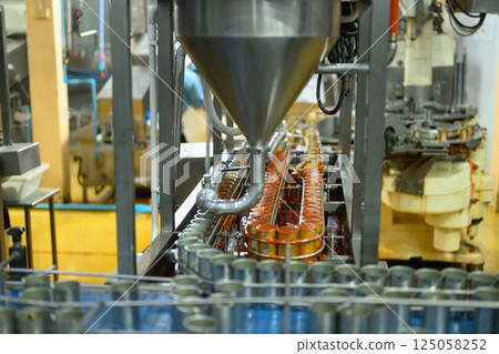 An industrial filling machine pouring sauce into cans at a modern canned fish production facility 125058252