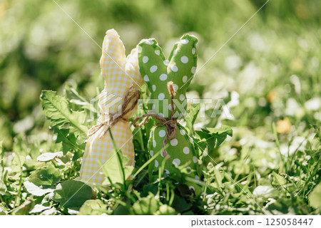 Handmade fabric Easter bunnies in yellow and green placed on vibrant green grass under bright spring sunlight 125058447