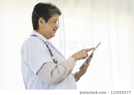 Confident senior female doctor using tablet computer standing in clinic. 125058577