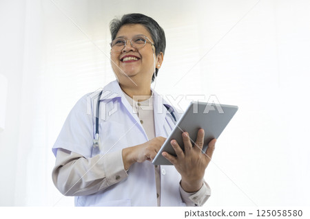 Confident senior female doctor using tablet computer standing in clinic. Confident senior female doctor using tablet computer standing in clinic. 125058580