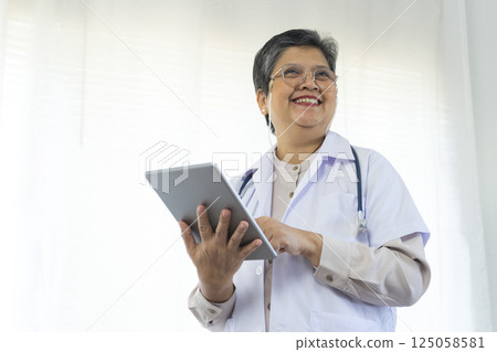 Confident senior female doctor using tablet computer standing in clinic. Confident senior female doctor using tablet computer standing in clinic. 125058581