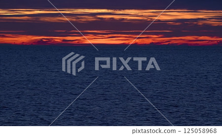 Sunlight glimmering across ocean waters, horizon burning with orange, red, and purple colors while gradually fading into deep nightfall and soft twilight shadows Sunlight glimmering across ocean waters, horizon burning with orange, red, and purple colors while gradually fading into deep nightfall and soft twilight shadows 125058968