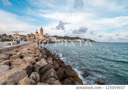 Rocky pier leading to the iconic church in Sitges, Spain 125059037
