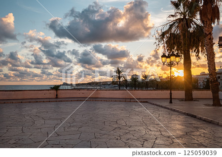 Dramatic sunset over the Mediterranean with a stone-paved terrace and palm trees 125059039