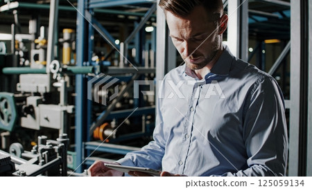 Industrial production facility with an engineer using a digital tablet, managing and controlling machinery, optimizing workflow, and ensuring smooth operations 125059134
