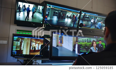 Security professional watching multiple surveillance monitors, tracking movement across building interior, maintaining vigilance and workplace safety 125059185