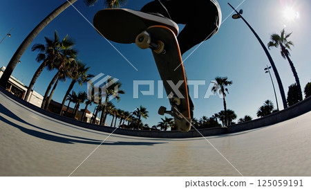 Skilled skateboarder executing aerial tricks at sunny urban skatepark, palm trees framing dynamic movement, highlighting skateboarding expertise with high energy motion capture 125059191