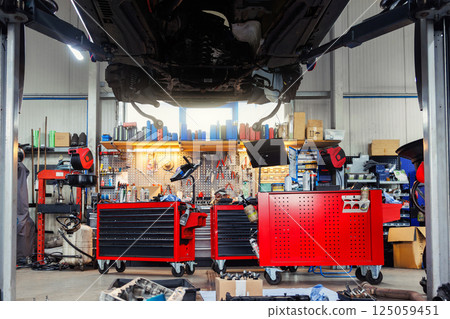 Scenic bottom POV disassembled SUV car with removed gearbox raised on lift elevator at workshop service maintenance station center. Vehicle check-up and repair. Underbody chassis and suspension parts Scenic bottom POV disassembled SUV car with removed gearbox raised on lift elevator at workshop service maintenance station center. Vehicle check-up and repair. Underbody chassis and suspension parts 125059451