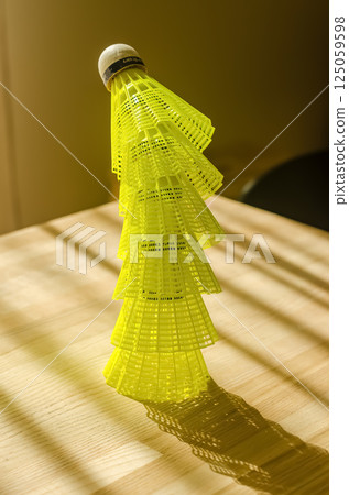 Neon yellow badminton shuttlecock with sharp shadows on sunlit wooden table. High quality photo 125059598