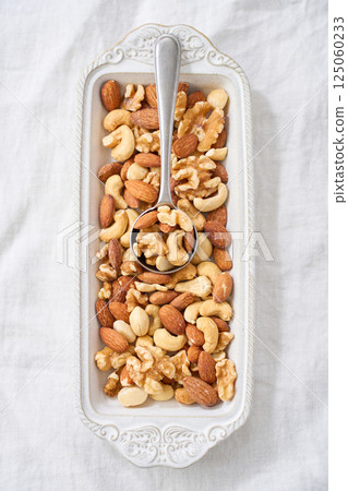 Mixed nuts in a white bowl and spoon 125060233