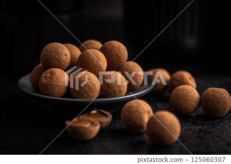 Chocolate truffles with cocoa powder and caramel filling on black table. 125060307
