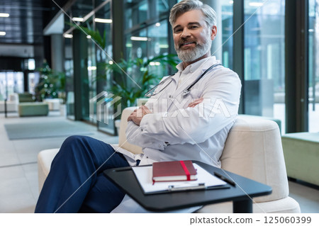 Smiling mature male doctor in lab coat looking positive and contented 125060399