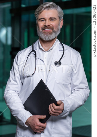 Mature male doctor in lab coat entering the clinic and looking determined 125060422