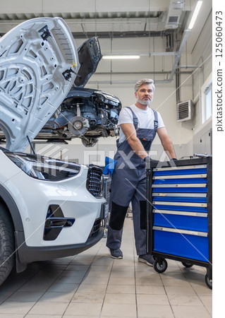 Bearded man auto mechanic with big tool box repairing automobile 125060473