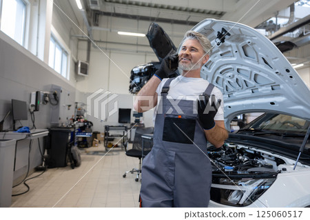 Professional technician car mechanic man in overalls using mobile cell phone talking with client 125060517