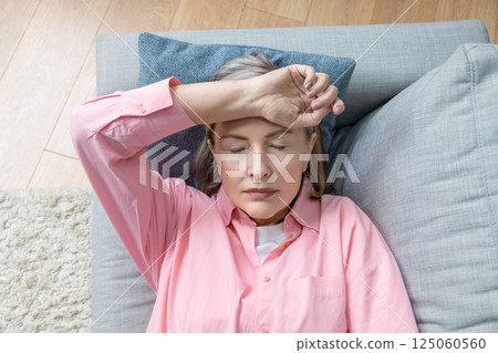 Senior caucasian woman in pink shirt lying on the bed and suffering form the headache Senior caucasian woman in pink shirt lying on the bed and suffering form the headache 125060560