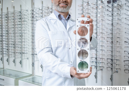Male doctor in the optic shop holding a lens color scale in hands Male doctor in the optic shop holding a lens color scale in hands 125061178