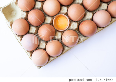 Fresh chicken brown eggs in a tray on a white background. Broken egg with yolk inside the shell. Fresh chicken brown eggs in a tray on a white background. Broken egg with yolk inside the shell. 125061662