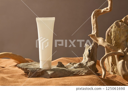 Cosmetics tube placed on a rough dark brown tree trunk, beneath a hot and dry sand field. Natural light shines on objects in the desert. Brightly colored tree roots twist into various shapes. Cosmetics tube placed on a rough dark brown tree trunk, beneath a hot and dry sand field. Natural light shines on objects in the desert. Brightly colored tree roots twist into various shapes. 125061698