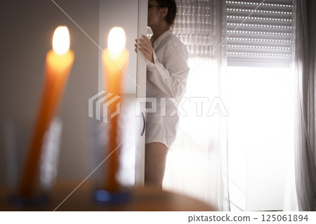 Woman hiding behind door with lit candles in foreground Woman hiding behind door with lit candles in foreground 125061894